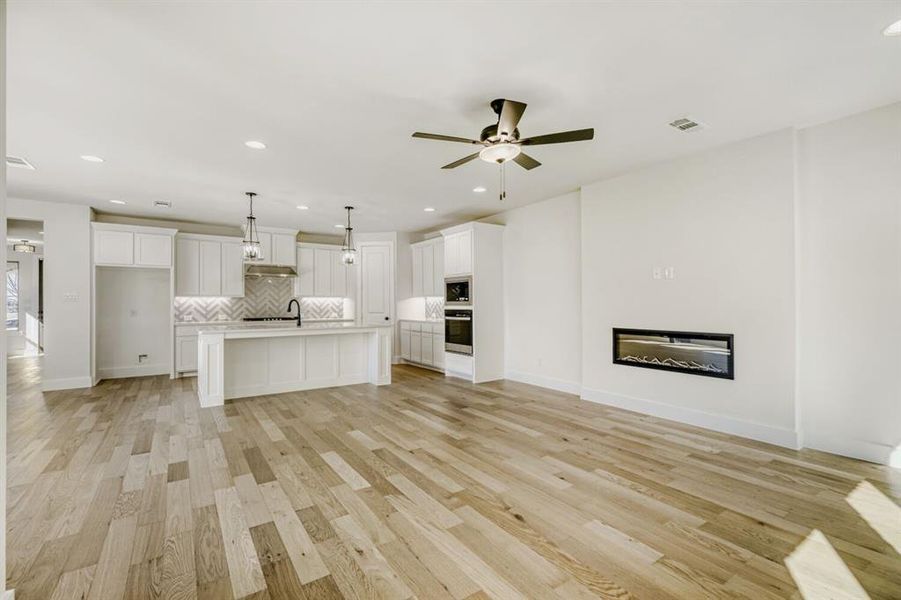 Unfurnished living room featuring recessed lighting, light wood-type flooring, a ceiling fan, and a glass covered fireplace
