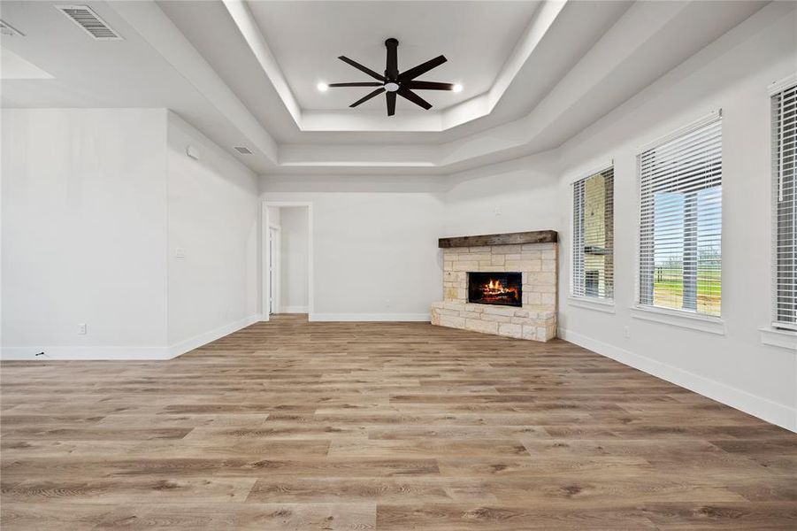 Unfurnished living room featuring a ceiling fan, light wood-style floors, a stone fireplace, and a raised ceiling