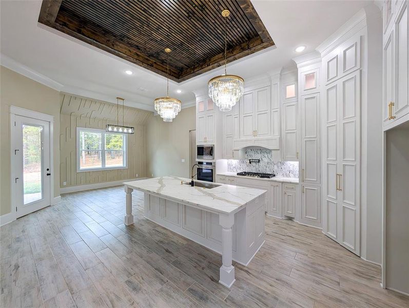 Kitchen with a kitchen bar, light stone counters, hanging light fixtures, an island with sink, and glass insert cabinets