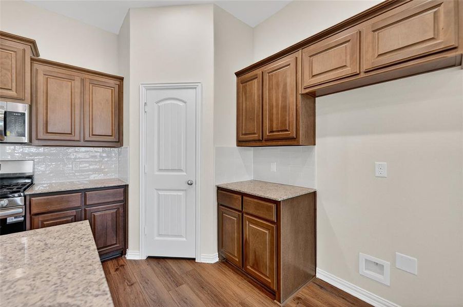Kitchen with light stone countertops, appliances with stainless steel finishes, dark wood-style floors, and brown cabinets