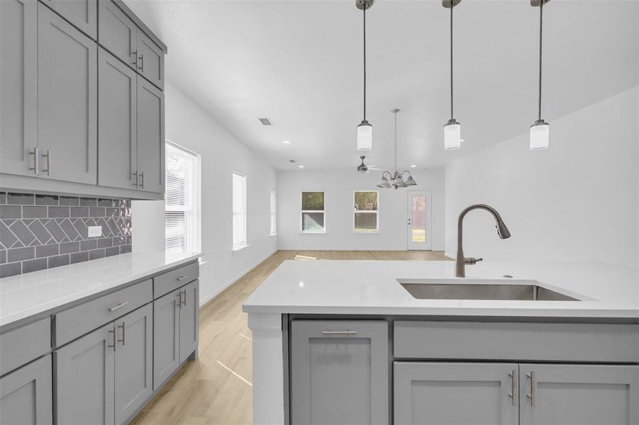 Kitchen with gray cabinetry, light wood finished floors, hanging light fixtures, and recessed lighting