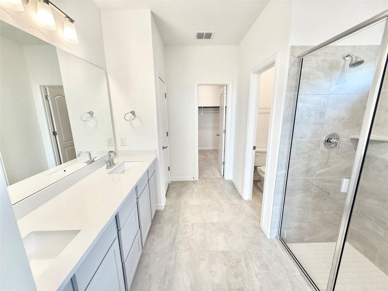 Full bath with a shower stall, double vanity, a spacious closet, and light tile patterned floors Full bath with a shower stall, double vanity, a spacious closet, and light tile patterned floors
