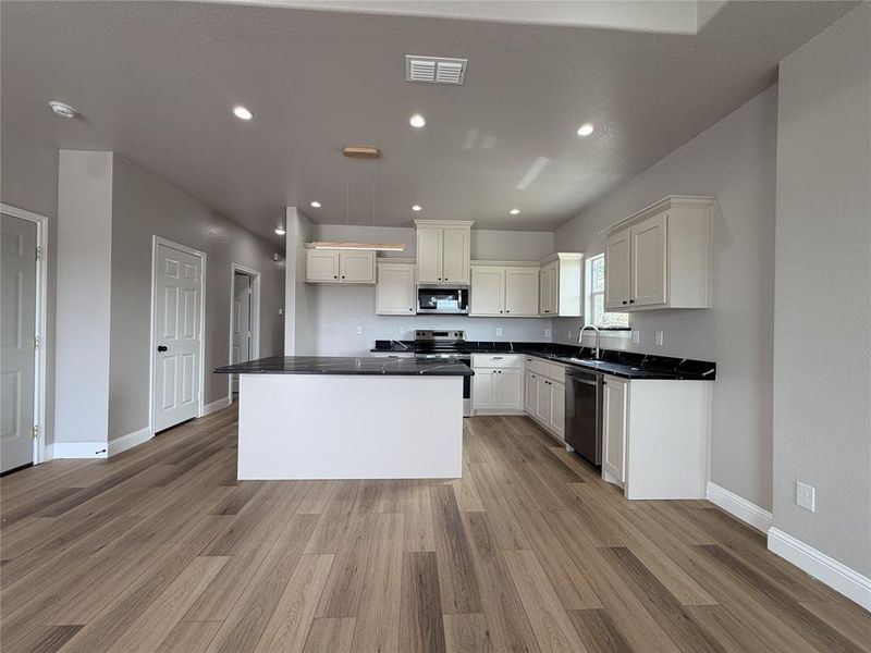 Kitchen with stainless steel appliances, a center island, white cabinets, light wood-style floors, and recessed lighting