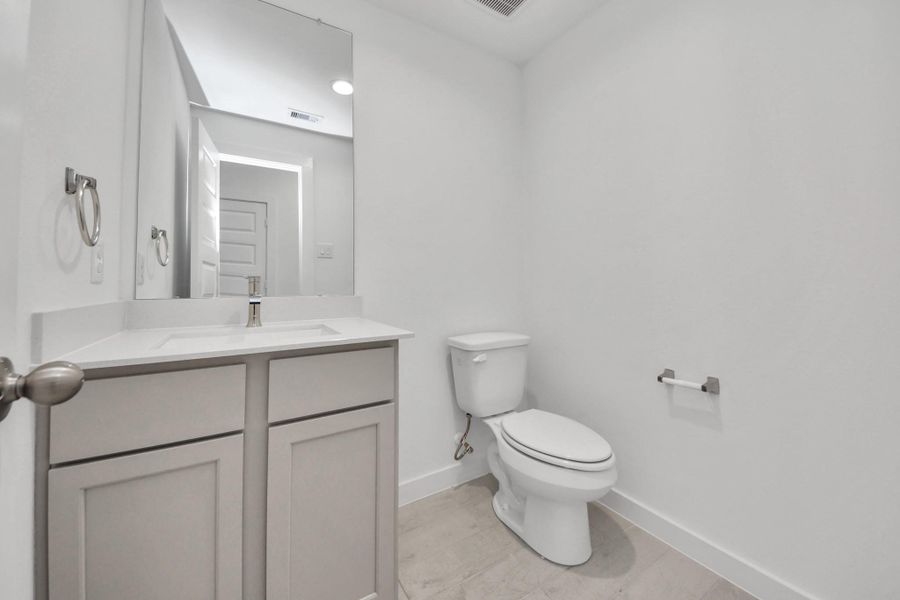 Sophisticated half bathroom adorned with contemporary finishes. The elegant 5-panel door welcomes you to a space where style meets functionality. Notice the sleek hardware accents that add a touch of modern charm. The vanity boasts light-colored countertops, beautifully complemented by a tasteful vanity light, creating a well-lit and inviting atmosphere. Sample photo of completed home with similar floor plan. Actual colors and selections may vary.