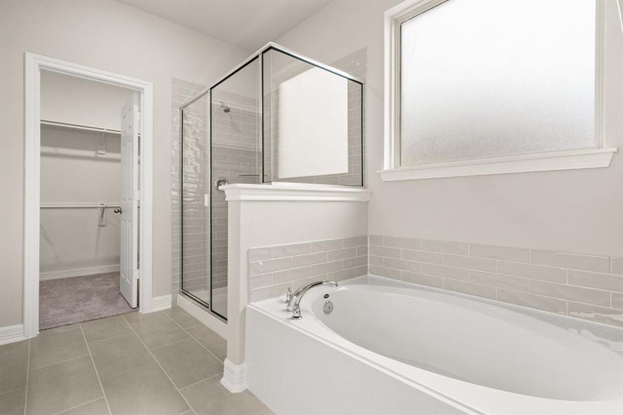 This additional view of your primary bathroom features tile flooring, fresh paint, walk-in shower, a separate garden tub, and a large walk-in closet.