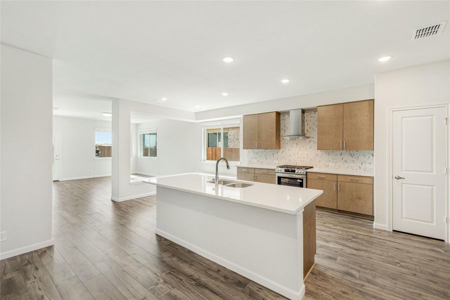 Open kitchen with large center island, wood cabinets, stainless range, and hardwood floors