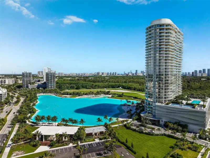 High-rise residential tower featuring wrap-around balconies, a crystalline swimming lagoon, landscaped grounds, and paved parking facilities