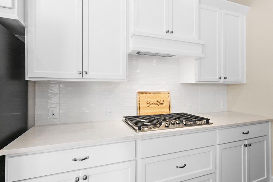 This modern kitchen features sleek white cabinetry, a stylish gas cooktop, and a clean, bright backsplash, offering a sophisticated and functional cooking space.