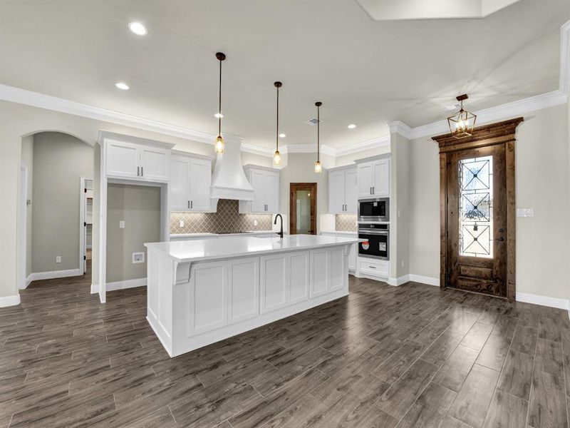 Kitchen featuring a kitchen island with sink, white cabinetry, stainless steel appliances, and premium range hood