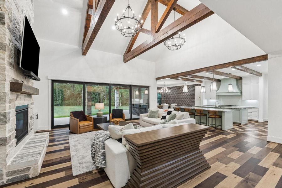 The dramatic great room showcases soaring 20-foot vaulted ceilings, exposed wood trusses, and a stunning stone fireplace with a raised hearth and custom mantel. Built-in cabinetry, floating shelves, and rich hardwood flooring create a warm yet sophisticated atmosphere, while oversized windows fill the space with natural light.