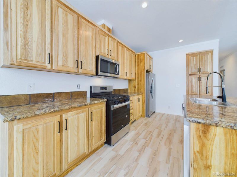 Kitchen with light counters, tile back splash, LVP floors, and maple cabinets.
