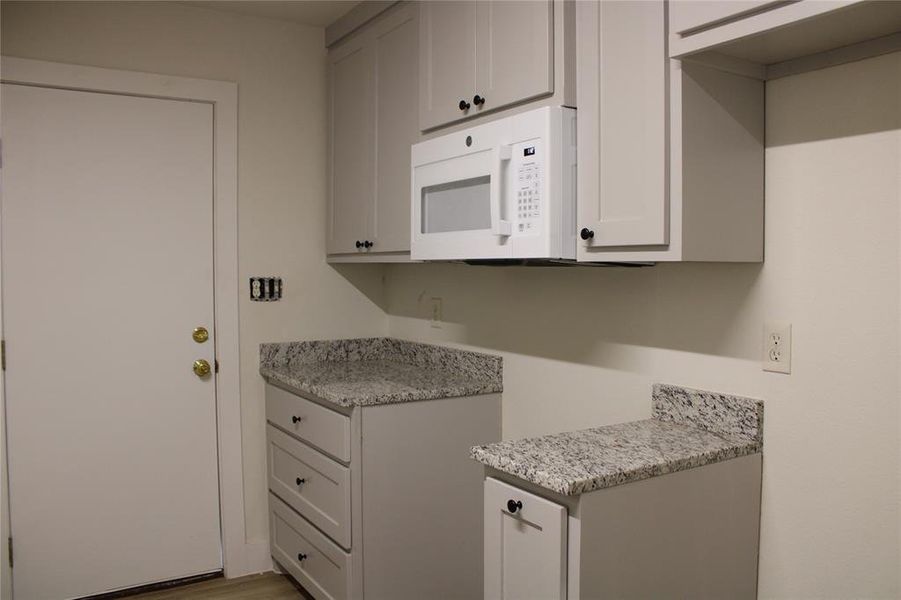 Kitchen featuring white microwave, light wood-style floors, light stone counters, and white cabinetry