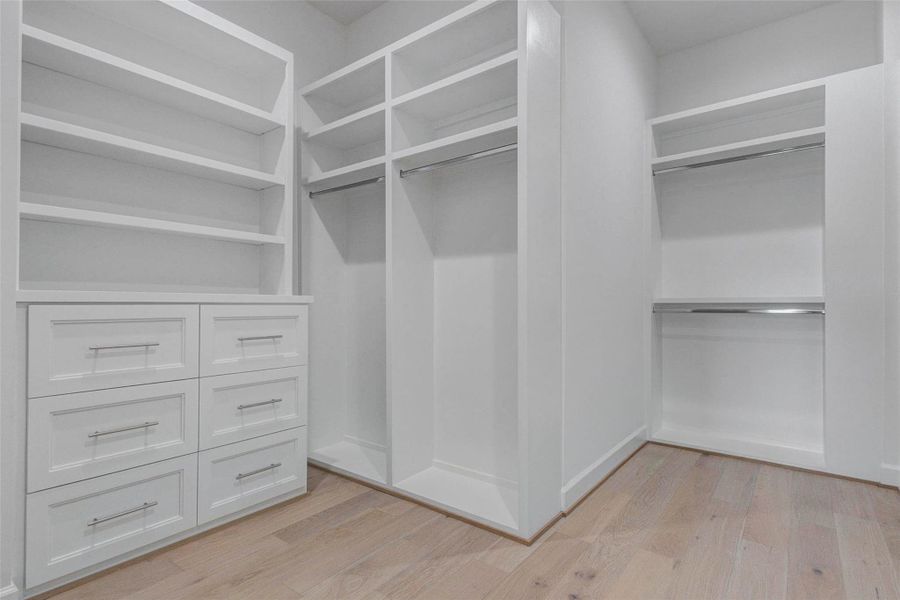 Detailed view of the custom closet system showcasing sleek hardware, integrated drawers, open shelving, and multiple hanging areas. The tailored layout maximizes storage efficiency while maintaining the home’s clean transitional-modern aesthetic. Wide-plank engineered wood flooring continues seamlessly into the space, elevating both function and design.