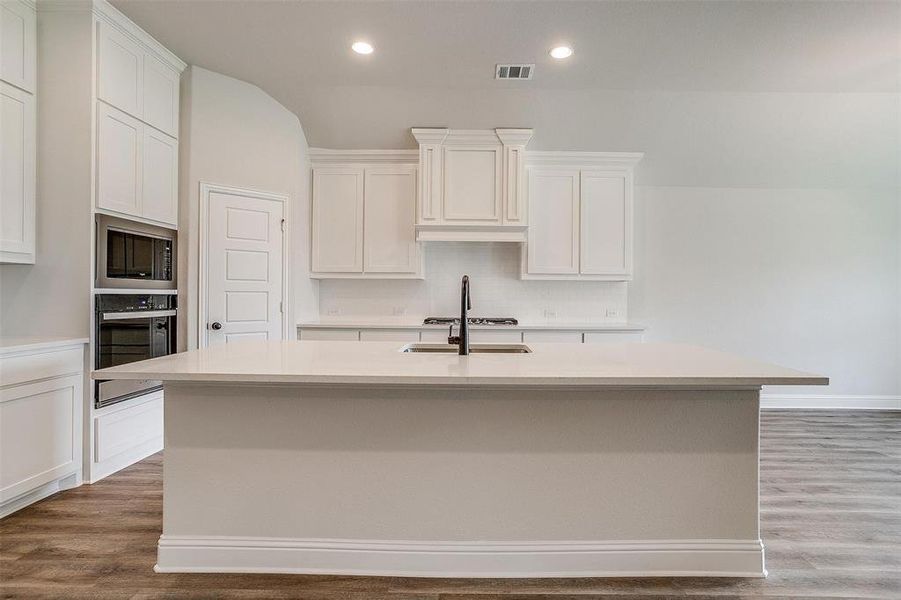 Kitchen featuring light wood-type flooring, black oven, and a kitchen island with sink