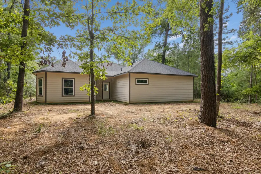 The back view is surrounded by trees, with a simple yard and a natural, wooded setting.