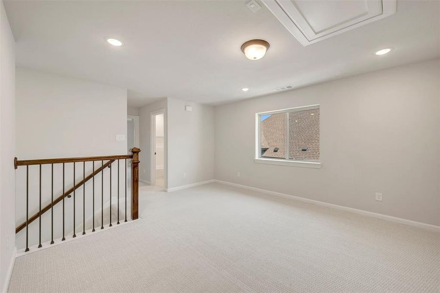 Upper-level landing featuring light-colored carpeting, a wood and iron baluster railing, recessed lighting, and a single window