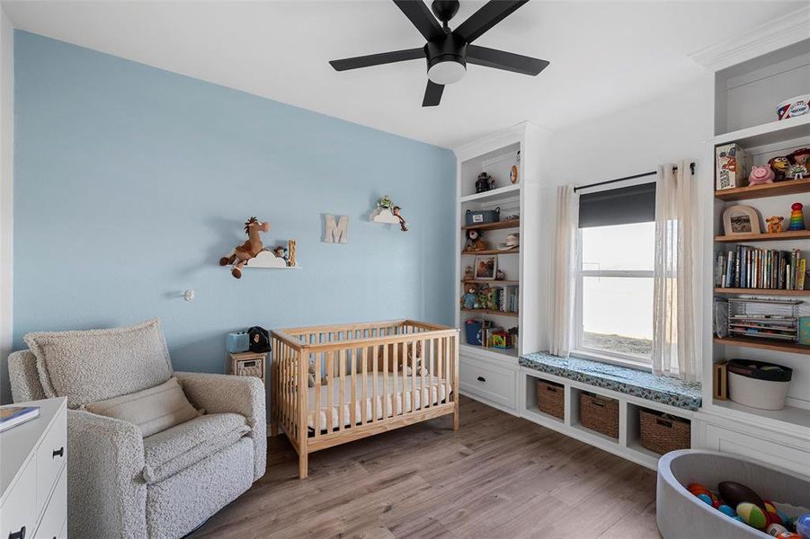 Bedroom featuring a crib, light wood-type flooring, and a ceiling fan