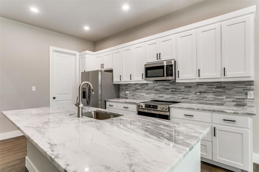 Kitchen with dark wood-type flooring, light stone countertops, and recessed lighting