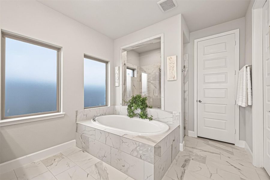 Exquisite primary bath showcasing sophisticated marble-patterned tile that encases the soaking tub and extends across the entire floor. (Note: Photo is staged; property is currently vacant.) Exquisite primary bath showcasing sophisticated marble-patterned tile that encases the soaking tub and extends across the entire floor. (Note: Photo is staged; property is currently vacant.)