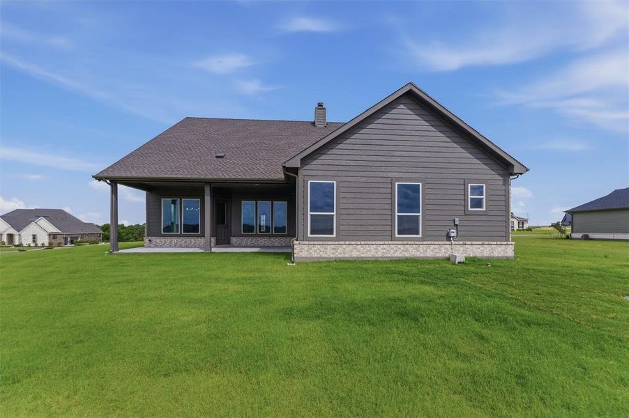Expansive green lawn bordering a single-story residence with dark gray siding and a light-colored stone accent foundation Expansive green lawn bordering a single-story residence with dark gray siding and a light-colored stone accent foundation
