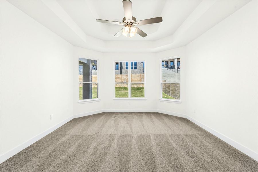 Carpeted empty room featuring a tray ceiling and a ceiling fan