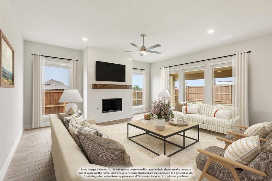 Bright living room with fireplace, wall-mounted TV, ceiling fan, and multiple windows with white curtains