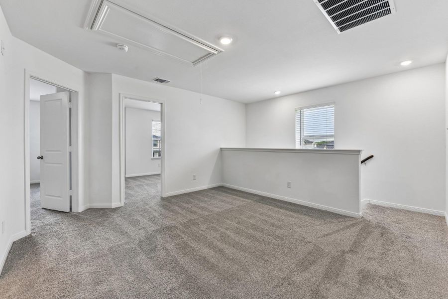 Spacious carpeted loft area featuring white walls, recessed lighting, a single window with blinds, and two doorways leading to additional rooms