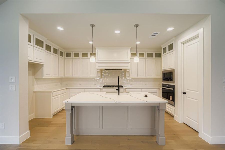 Kitchen featuring backsplash, recessed lighting, hanging light fixtures, a center island with sink, and a breakfast bar area