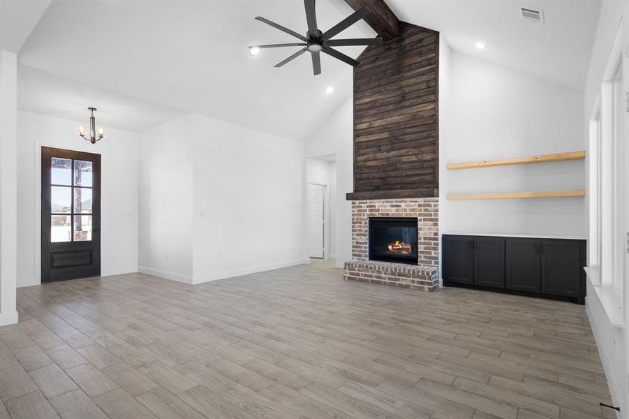 Unfurnished living room featuring hardwood / wood-style flooring, a fireplace, ceiling fan with notable chandelier, and beam ceiling