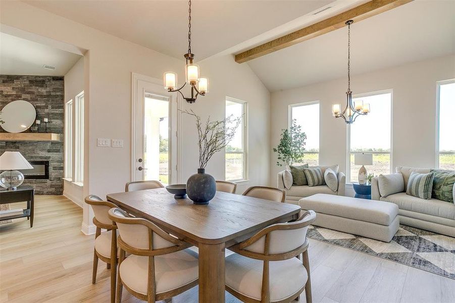 Dining space featuring an inviting chandelier, a stone fireplace, lofted ceiling with beams, and light hardwood / wood-style floors