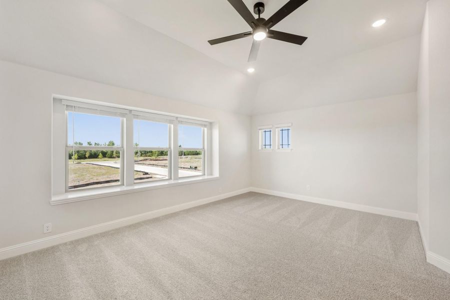 Empty bedroom with vaulted ceiling, ceiling fan, carpet flooring, and large windows overlooking a yard Empty bedroom with vaulted ceiling, ceiling fan, carpet flooring, and large windows overlooking a yard