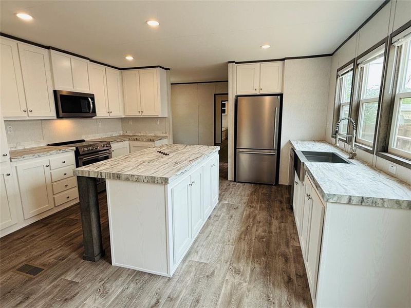 Kitchen with wood finished floors, stainless steel appliances, a kitchen island, light countertops, and a sink