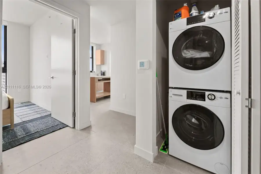 Stacked white front-loading laundry units with integrated digital controls and neutral-tone tile flooring