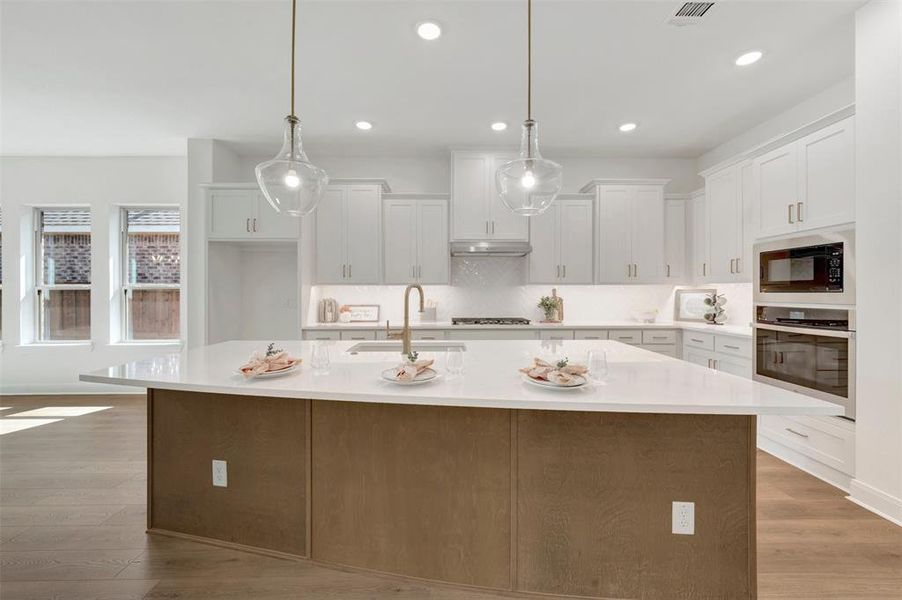 Modern kitchen featuring a large central island with a light-toned countertop and wood-finish paneling, under-cabinet lighting, ceiling-mounted recessed lighting, stainless steel appliances, and wood-finish flooring Modern kitchen featuring a large central island with a light-toned countertop and wood-finish paneling, under-cabinet lighting, ceiling-mounted recessed lighting, stainless steel appliances, and wood-finish flooring