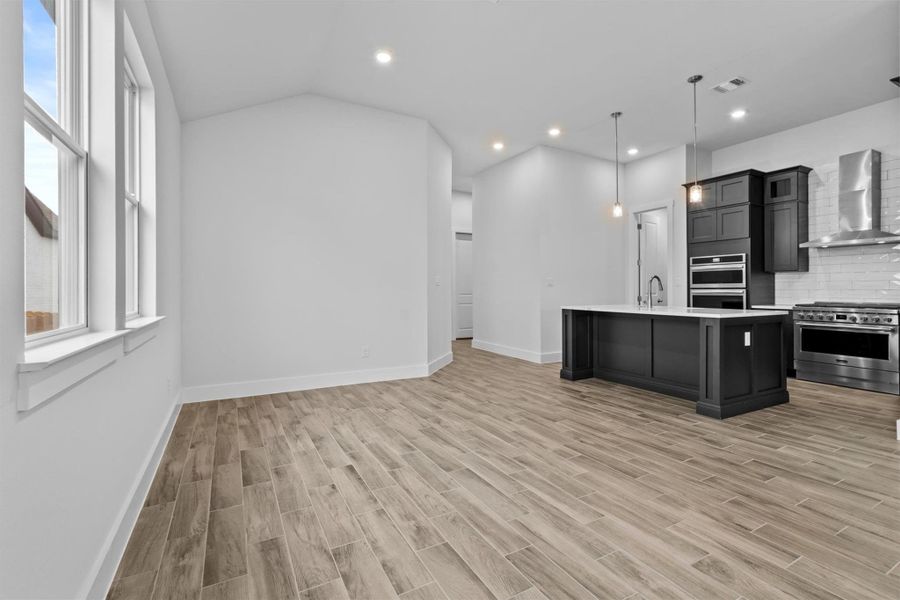 Kitchen with appliances with stainless steel finishes, tasteful backsplash, a kitchen island with sink, decorative light fixtures, and wall chimney range hood