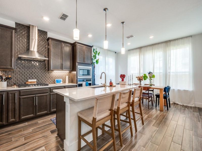 Kitchen with wall chimney exhaust hood, stainless steel appliances, dark brown cabinets, light wood-style flooring, and recessed lighting