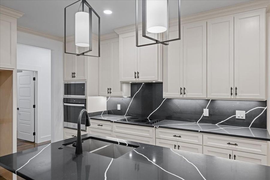 Kitchen featuring stainless steel appliances, dark counters, tasteful backsplash, off-white cabinets, and ornamental molding Kitchen featuring stainless steel appliances, dark counters, tasteful backsplash, off-white cabinets, and ornamental molding