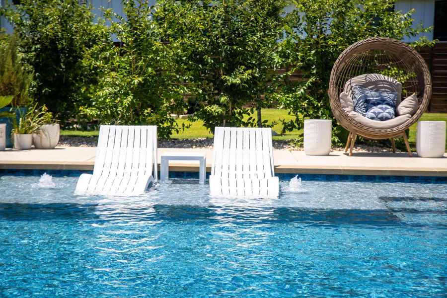 An inviting pool area with in-water lounge seating and serene garden surroundings beckons for relaxation.