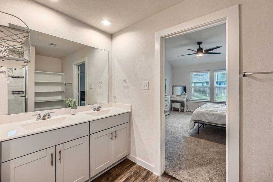 Bathroom featuring baseboards, a sink, ceiling fan, double vanity, and ensuite bath