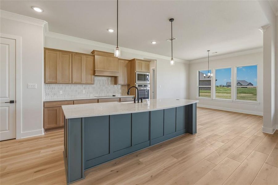 Spacious kitchen featuring a large central island with a light-toned countertop, wood-finish flooring, and light natural wood cabinetry Spacious kitchen featuring a large central island with a light-toned countertop, wood-finish flooring, and light natural wood cabinetry