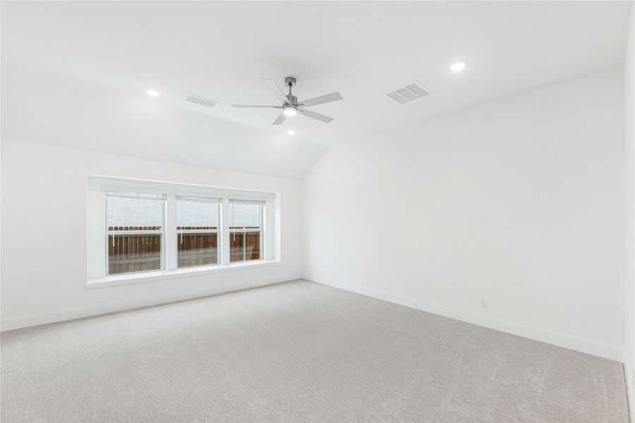 Empty bedroom with vaulted ceiling, ceiling fan, carpet flooring, and large triple window