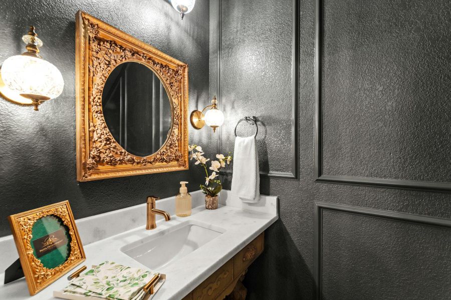 Powder room featuring a decorative gold-framed mirror, a single vanity with a white countertop, and a brass-finish faucet