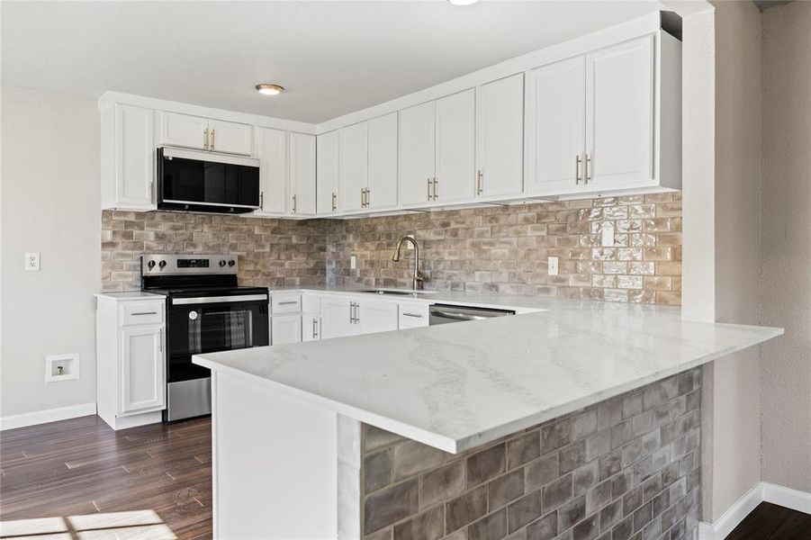 Kitchen featuring stainless steel appliances, a peninsula, white cabinetry, and light countertops