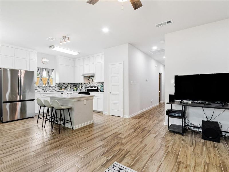 Open-concept living space featuring wood-finish flooring, a contemporary kitchen, white cabinetry, a kitchen island with seating, and stainless steel appliances