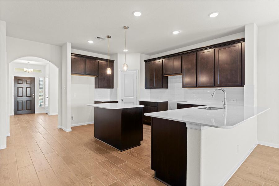 Another angle of the stunning open concept layout highlighting the seamless flow from the entry toward the gourmet kitchen and main living spaces. The beautiful wood looking tile flooring ties the entire first floor together while the large kitchen island becomes a focal point for gatherings and everyday living.