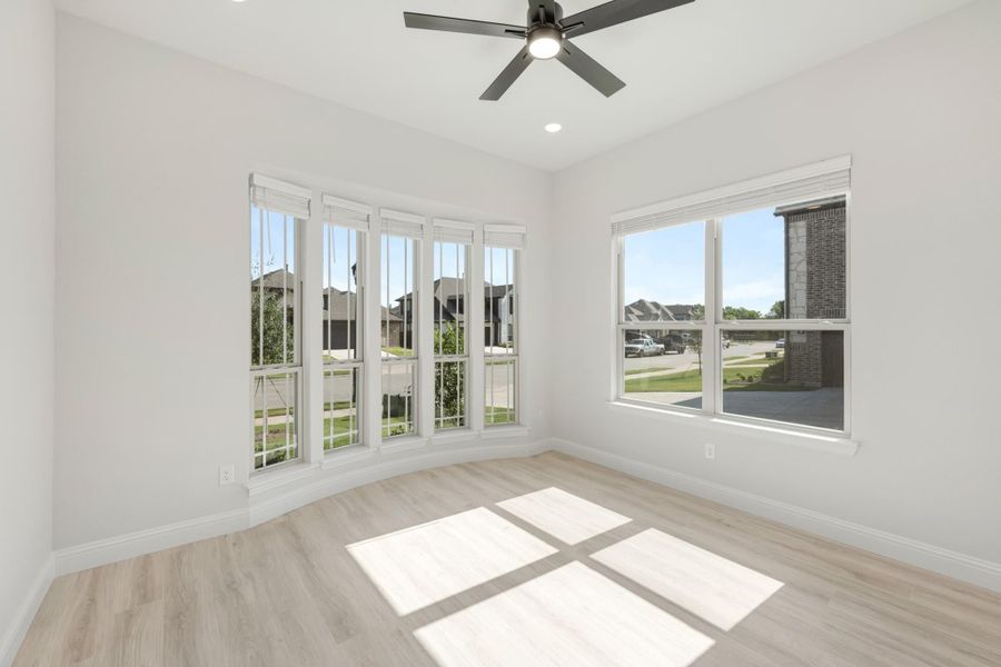 Empty room with light wood floors, ceiling fan, and large windows overlooking a neighborhood