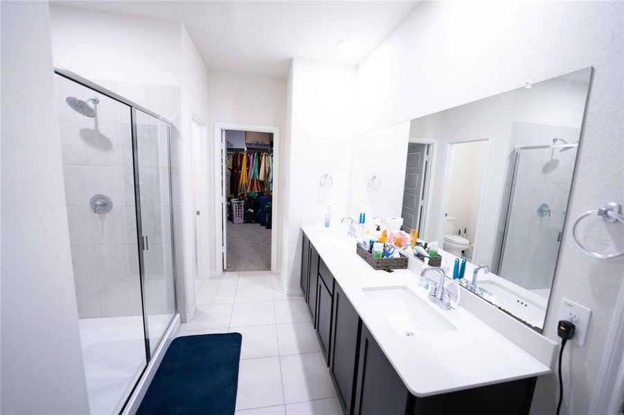 Spacious bath featuring a double vanity with white countertops, dark cabinetry, and a large frameless mirror Spacious bath featuring a double vanity with white countertops, dark cabinetry, and a large frameless mirror