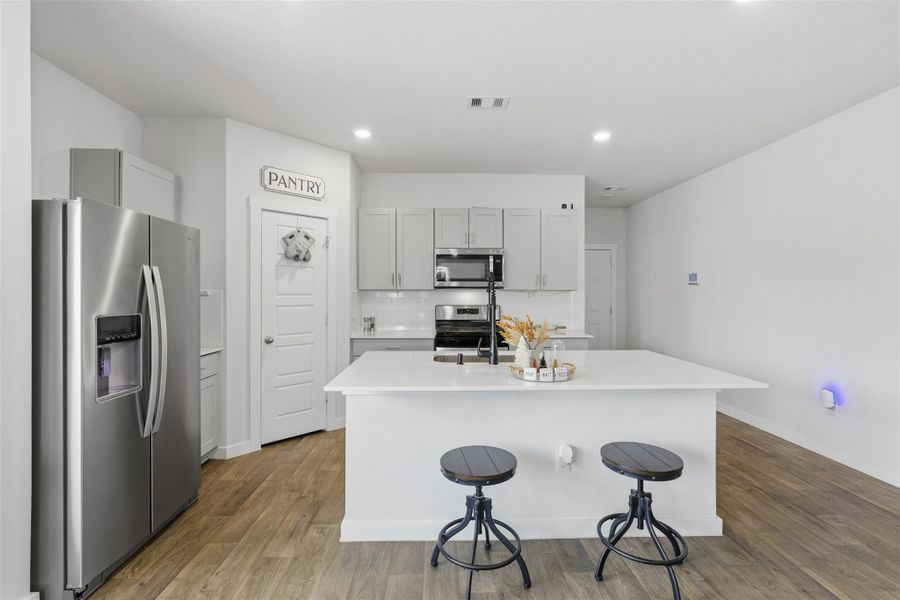 Kitchen featuring appliances with stainless steel finishes, a center island with sink, a breakfast bar area, light wood-style flooring, and backsplash