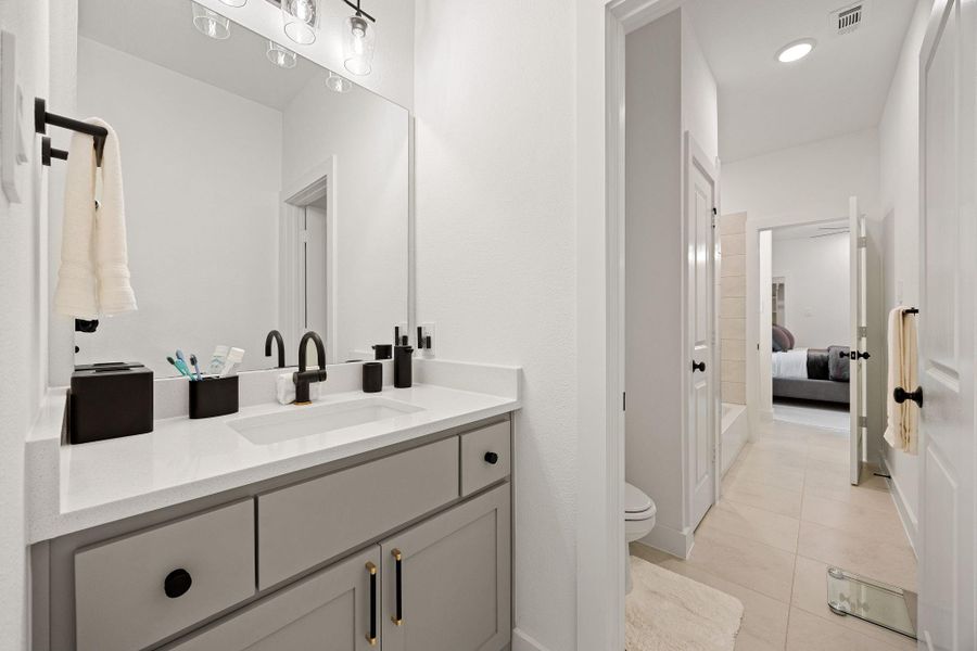 This modern jack and jill bathroom provide a sleek vanity, black fixtures, and ample lighting. The space includes a large mirror, a shower, and connects to a bedroom, providing a seamless flow.