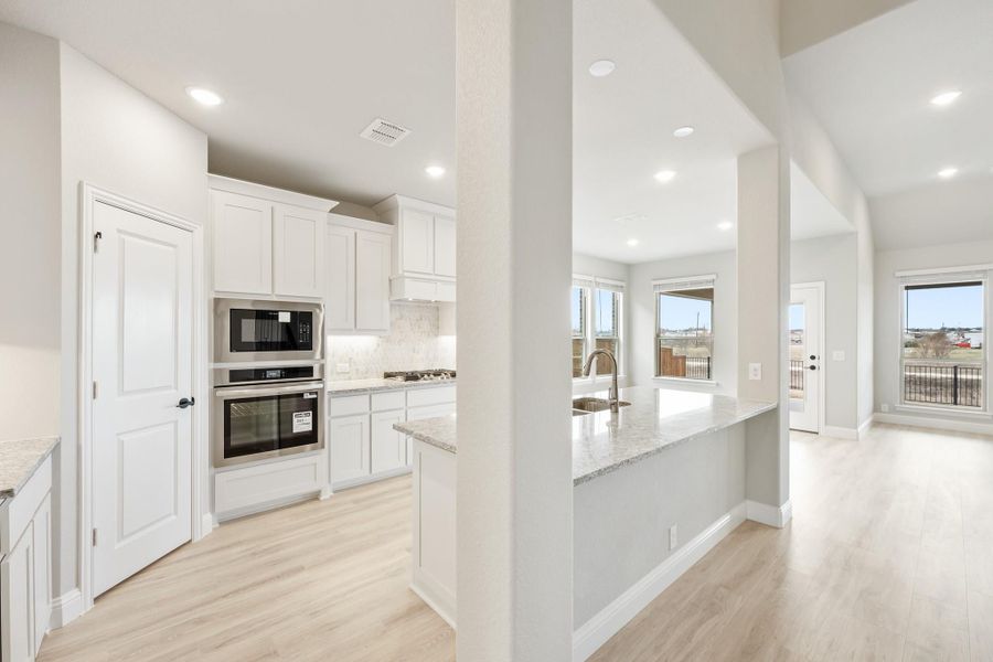 Open kitchen with white cabinets, stainless steel appliances, granite island with sink, and light wood floors Open kitchen with white cabinets, stainless steel appliances, granite island with sink, and light wood floors
